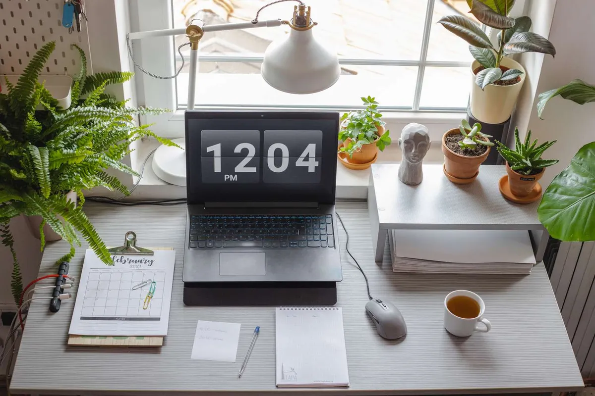 A windowsill lined with small pots beside a desk with a calendar and a laptop.