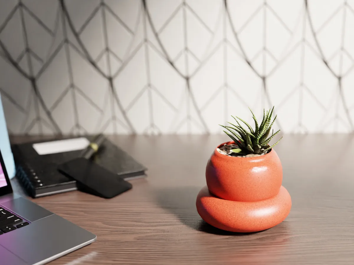 A small, rounded terracotta-orange pot with a succulent, sitting beside a laptop on a wooden desk.
